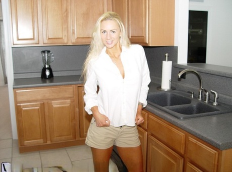 Blonde girl cups her huge boobs while getting naked in the kitchen