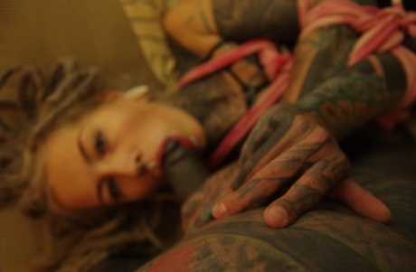 Heavily tattooed female sucks a black cock and masturbates while tied up