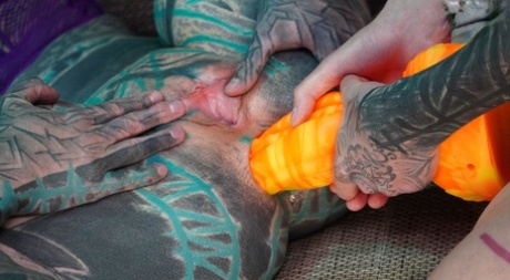 Heavily tattooed girls engage in anal play during GGB sex on a sofa