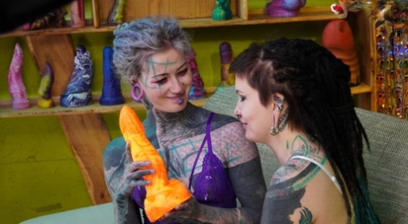 Heavily tattooed girls engage in anal play during GGB sex on a sofa